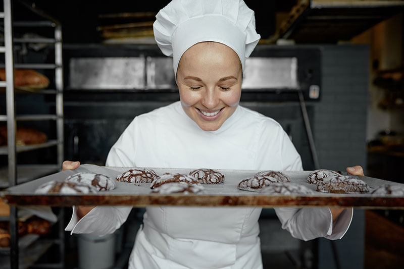 feliz panadero sonriente con bandeja de galletas recien horneadas en la cocina de la panaderia
